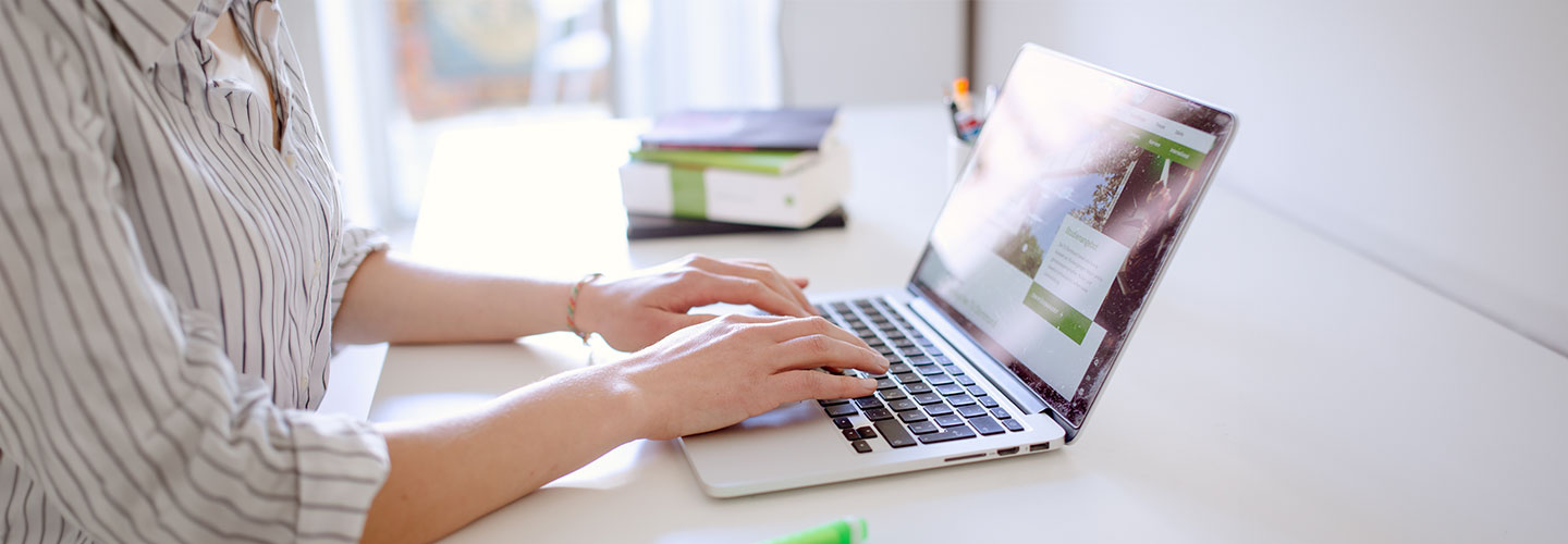 Studentin tippend am Laptop, daneben liegen Bücher und Stifte.